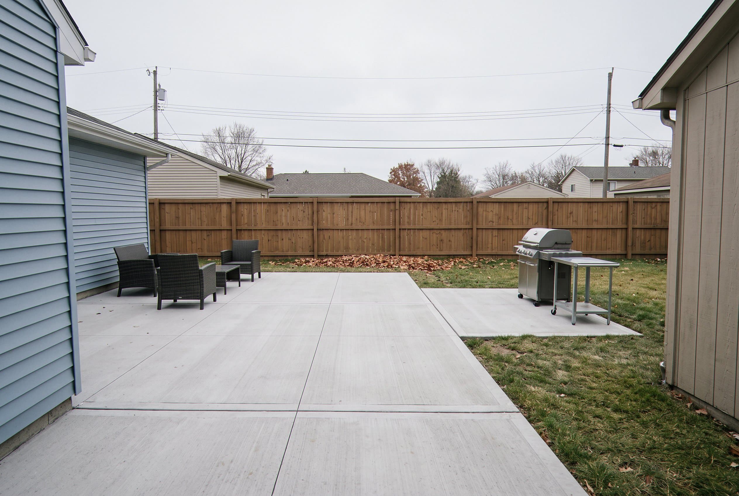 Backyard concrete patio with seating and a grill